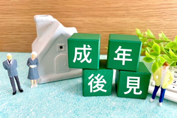 「成年後見」の積み木と家の模型を囲むミニチュア人形と電卓
