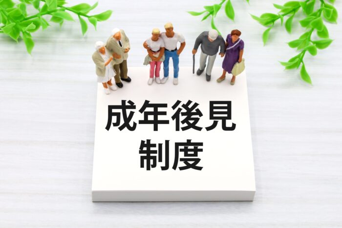 「成年後見制度」と書かれたブロックの上に立つ高齢者と介助者のミニチュア人形