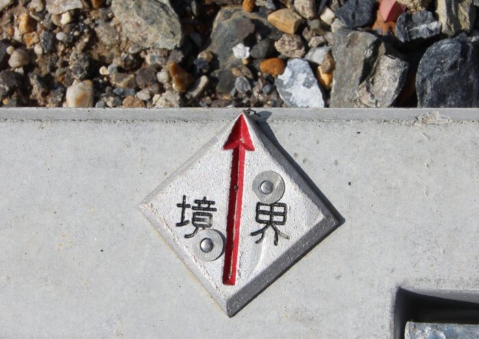 赤い矢印で境界位置を示す金属製の境界標鋲