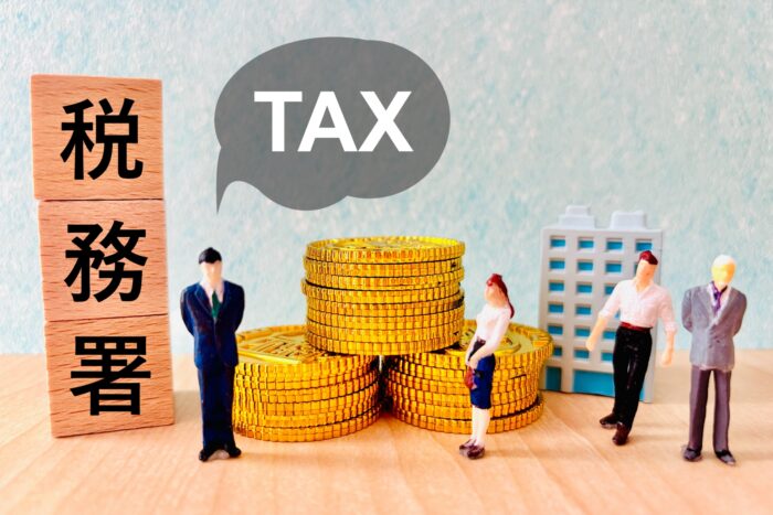 「税務署」「TAX」の文字と硬貨の山の前に立つ人形|ふるさと納税と併用できる節税制度